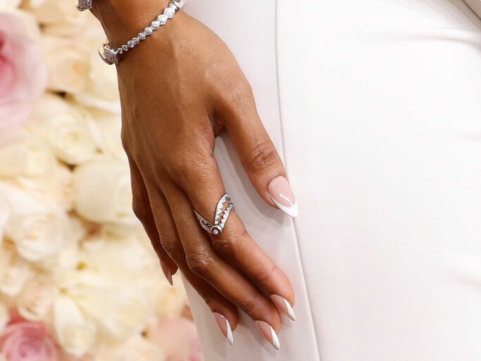 Hand mit French Nails wird vor einem beigen Kleid gehalten | © Getty Images/Taylor Hill 