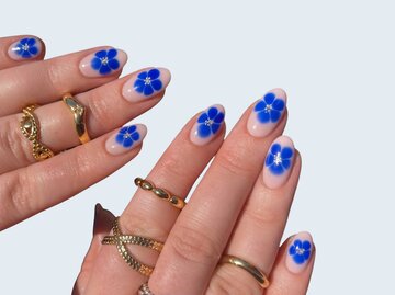 Hände mit goldenen Ringen und Nägeln mit blauen Blumen | © Adobe Stock/Helmy