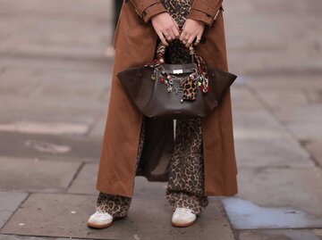 Beinansicht eine jungen Frau, die eine Leoparden-Jeans, Sneaker und einen braunen Mantel trägt. In den Händen hält sie eine große Tasche. | © Getty Images/Jeremy Moeller