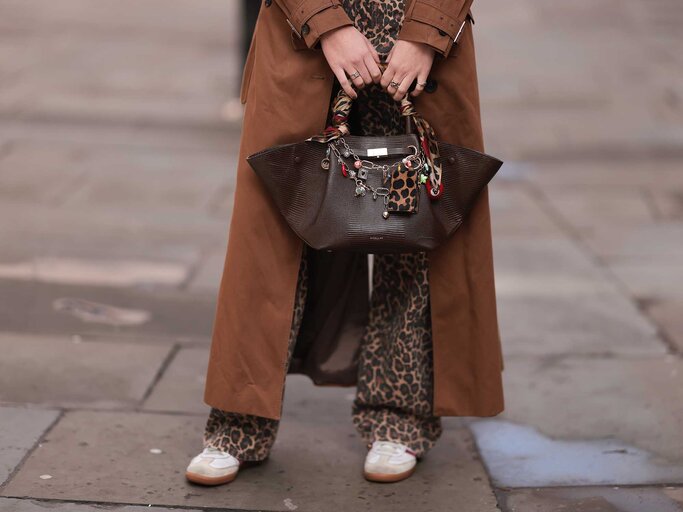 Beinansicht eine jungen Frau, die eine Leoparden-Jeans, Sneaker und einen braunen Mantel trägt. In den Händen hält sie eine große Tasche. | © Getty Images/Jeremy Moeller