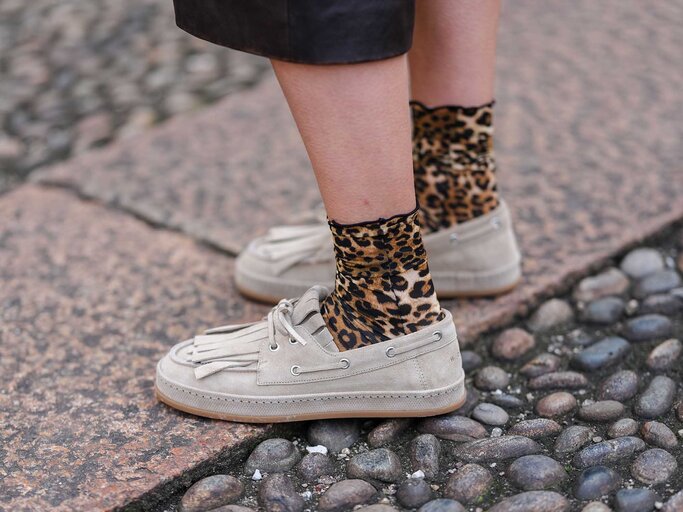 Frau trägt beige Bootsschuhe mit Leoparden-Socken auf der Straße. | © Getty Images/Edward Berthelot