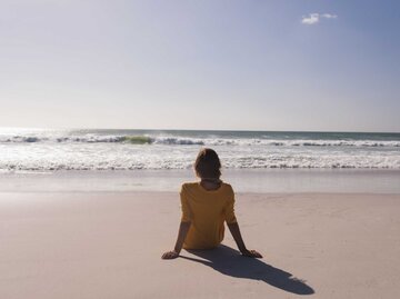 Frau sitzt am Strand und schaut aufs Meer | © Adobe Stock/wavebreak3