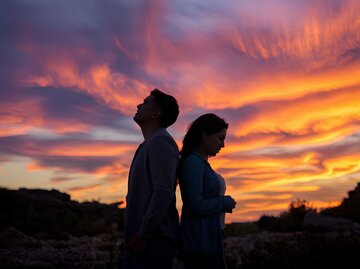 Paar steht Rücken and Rücken vor einem Sonnenuntergang | © Adobe Stock/NASSRI