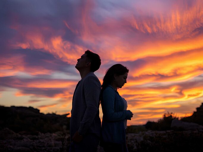 Paar steht Rücken and Rücken vor einem Sonnenuntergang | © Adobe Stock/NASSRI