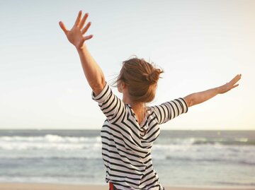 Frau streckt glücklich die Arme aus und schaut aufs Meer | © Adobe Stock/JenkoAtaman