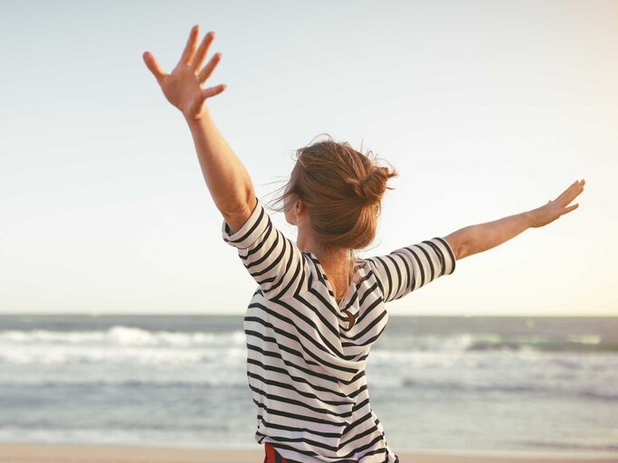 Frau streckt glücklich die Arme aus und schaut aufs Meer | © Adobe Stock/JenkoAtaman