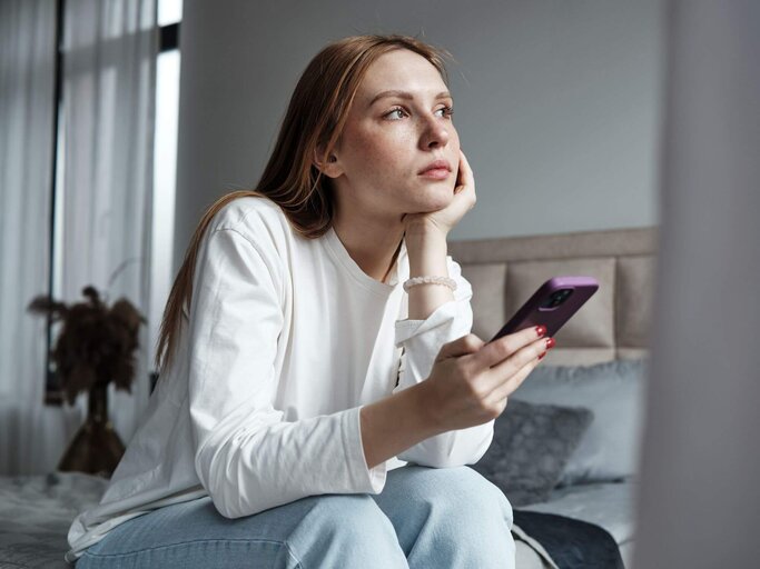 Person sitzt mit Handy auf Bett | © Getty Images/MementoJpeg