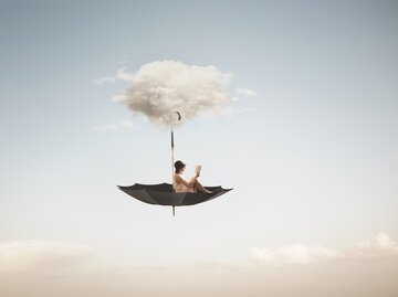 Frau liest ein Buch auf einem umgestürzten Regenschirm in den Wolken, Fantasiewelt | © GettyImages/	fcscafeine