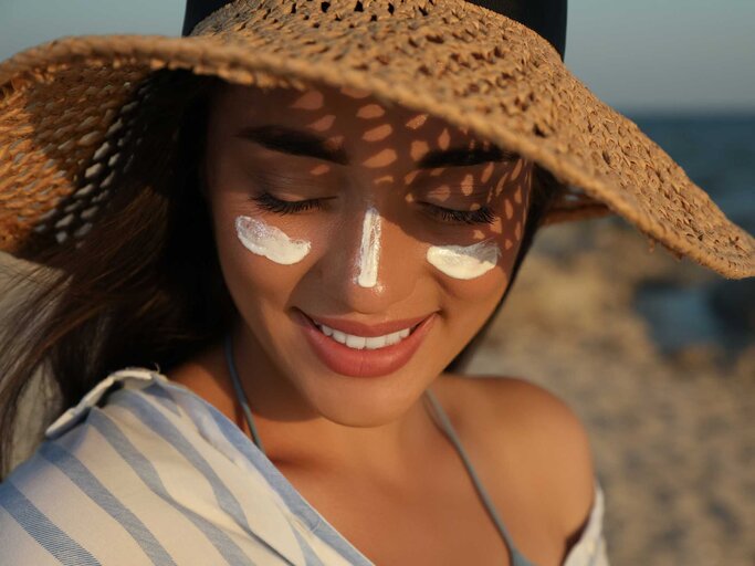 Glückliche Frau mit Hut und Sonnencreme | © Getty Images/Liudmila Chernetska