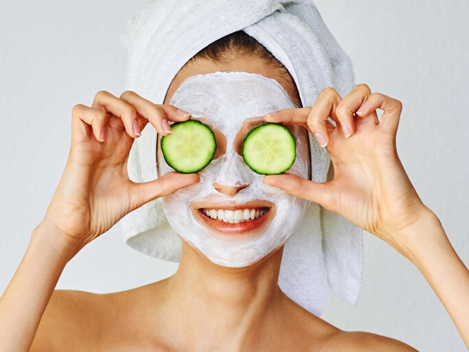 Frau trägt eine Gesichtsmaske und hält sich zwei Gurkenscheiben vor die Augen | © Getty Images/Olesia Bekh