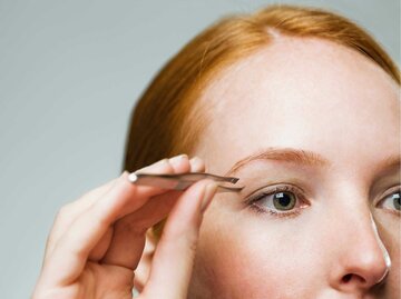 Frau zupft mit einer Pinzette ihre roten Augenbrauen. | © Getty Images/Compassionate Eye Foundation/David Oxberry/OJO Images Ltd