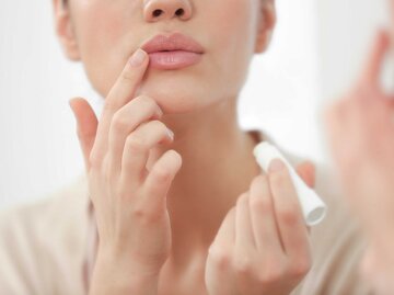 Frau trägt Lippenpflege auf ihre Lippen mit dem Finger auf | © Adobe Stock/Africa Studio