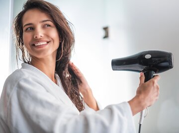 Frau in weißem Bademantel föhnt sich die Haare | © AdobeStock/Yakobchuk Olena