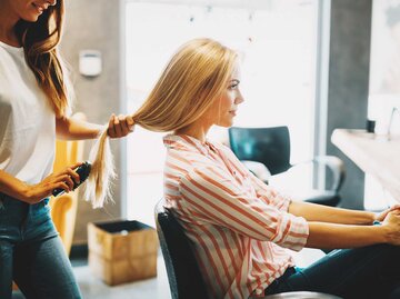 Eine Frau wird von einer Friseurin bei ihren Haaren beraten | © Adobe Stock/NDABCREATIVITY