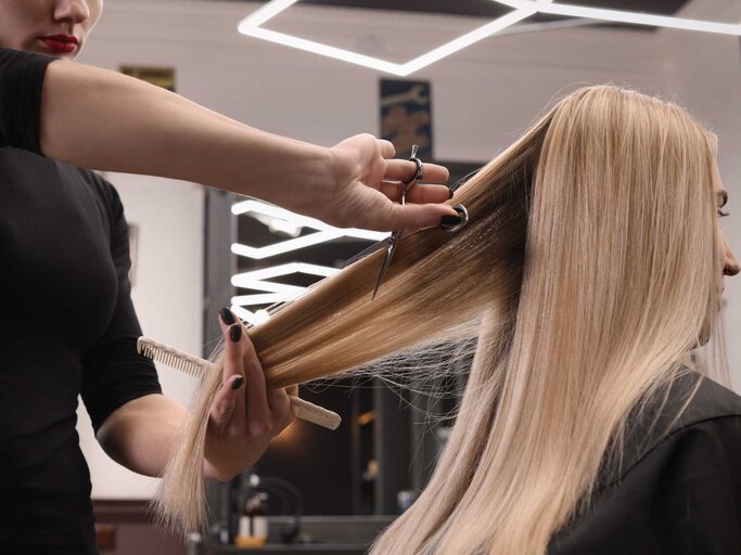 Blonde Frau sitzt auf dem Friseurstuhl und bekommt Haare geschnitten | © Adobe Stock/New Africa