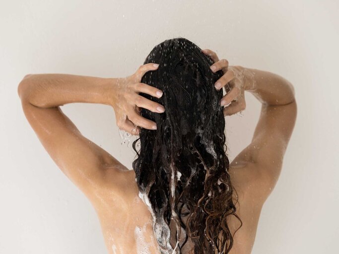 Frau wäscht sich unter der Dusche die langen Haare | © Adobe Stock/fizkes