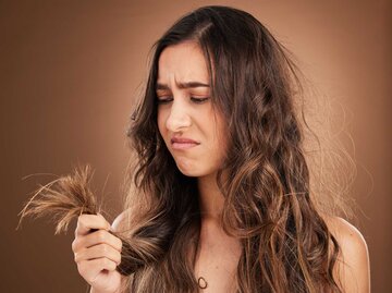 Frau schaut frustriert auf ihre Haare | © Adobe Stock/ D Theron/peopleimages.com