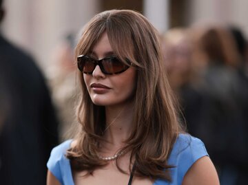 Frau mit Pony-Frisur und Sonnenbrille in einem blauen Kleid | © Getty Images/Jeremy Moeller 