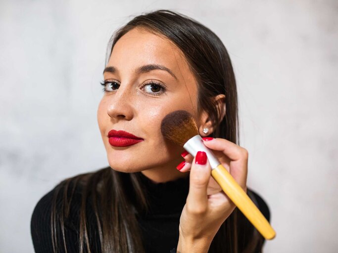 Frau trägt Rouge mit einem Pinsel auf. | © Getty Images/Aleksandar Jankovic