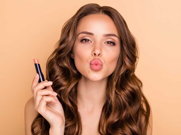 Frau macht einen Kussmund und hält einen Lippenstift in der Hand | © Adobe Stock/deagreez