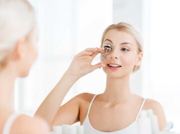 Frau benutzt eine Wimpernzange | © Adobe Stock/Syda Productions