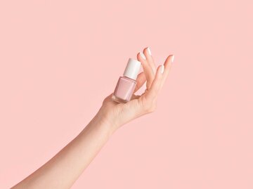 Hand einer jungen Frau, die eine Nagellack-Flasche auf ihrer Hand balanciert | © Adobe Stock/Prostock-studio