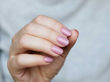 Hand mit lila lackierten Fingernägeln | © Getty Images/Mariia Demchenko
