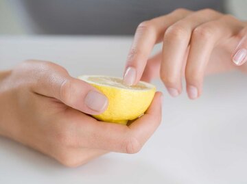 Hand mit lackierten Fingernägeln hält eine Zitrone fest | © Getty Images/Cecile Lavabre