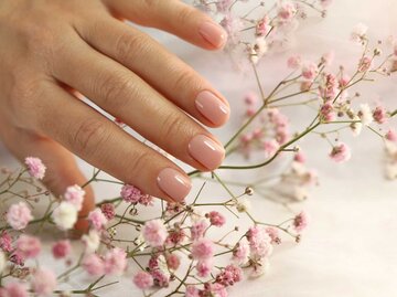 Rosa lackierte Fingernägel vor einem Ast mit Blumen | © Getty Images/marigo20