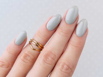 Finger mit grauem Nagellack und goldenen Ringen | © Adobe Stock/Darya Lavinskaya