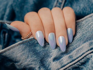 Frau trägt Jeansjacke und hat blaue Chrome Nails an ihrer Hand | © Adobe Stock/Dmitri