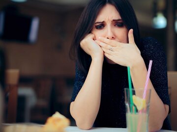 Frau sitzt im Restaurant am Tisch und hat Schluckauf. | © Getty Images / nicoletaionescu