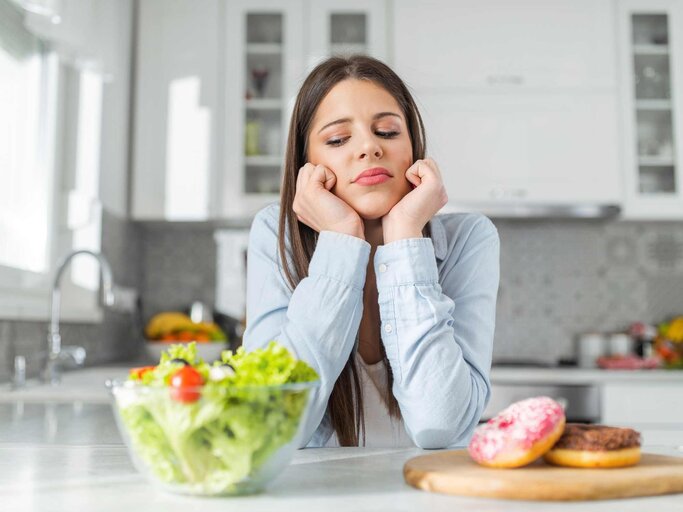 Junge Frau wählt zwischen Donuts und Gemüsesalat | © Getty Images/bulatovic