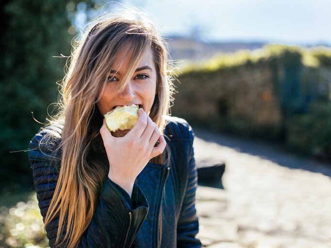 Eine junge Frau mit Lederjacke beißt in einem Apfel | © GettyImages/Westend61