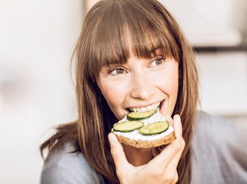 Junge Frau beisst in ein Brot mit Frischkäse und Gurke | © Getty Images/Westend61