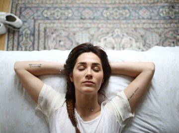 Frau liegt mit geschlossenen Augen auf dem Bett. | © Getty Images/Catherine Delahaye