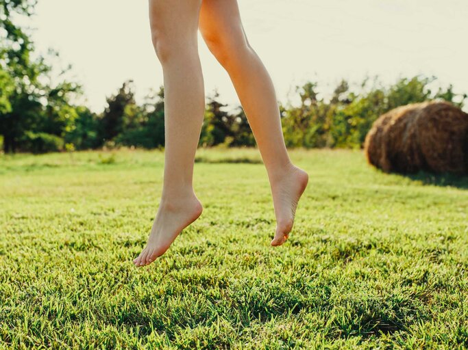Nahaufnahme von nackten Füßen, die über einer grünen Wiese schweben | © Adobe Stock/Bostan Natalia