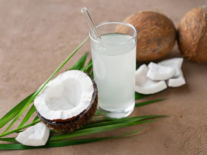 Glas Kokoswasser, Kokosnüssen und Palmblatt | © GettyImages/Kristina Ratobilska