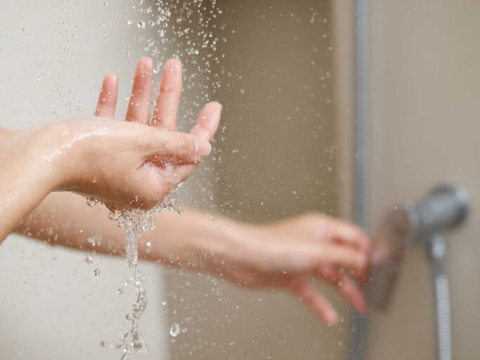 Person hält Hand unter das Wasser beim Duschen | © Adobe Stock/methaphum