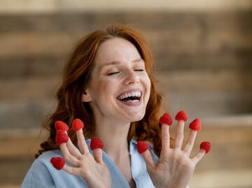 Lachende Frau mit Himbeeren auf den Fingern. | © Getty Images/Westend61