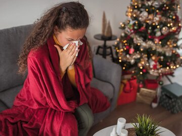 Frau krank auf Sofa vor Weihnachtsbaum | © Getty Images/Dobrila Vignjevic