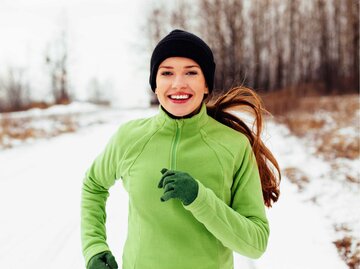 Junge Frau joggt lachend durch den Schnee. | © Getty Images/BartekSzewczyk