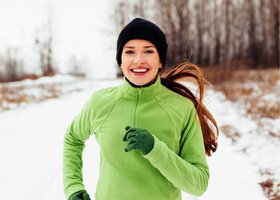 Junge Frau joggt lachend durch den Schnee.