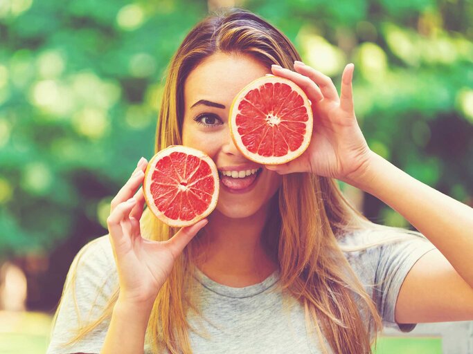 Frau hält sich zwei halbe Grapefruits vors Gesicht. | © Adobe Stock/Tierney