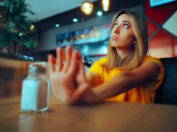 Frau sitzt am Tisch und sagt "Nein" zu Salz. | © Adobe Stock/nicoletaionescu