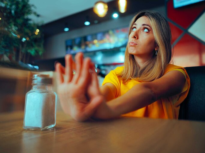 Frau sitzt am Tisch und sagt "Nein" zu Salz. | © Adobe Stock/nicoletaionescu