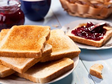 Auf einem Frühstückstisch liegen viele Scheiben Toastbrot auf einem Teller, eine ist mit Marmelade bestrichen. | © Adobe Stock/gkrphoto