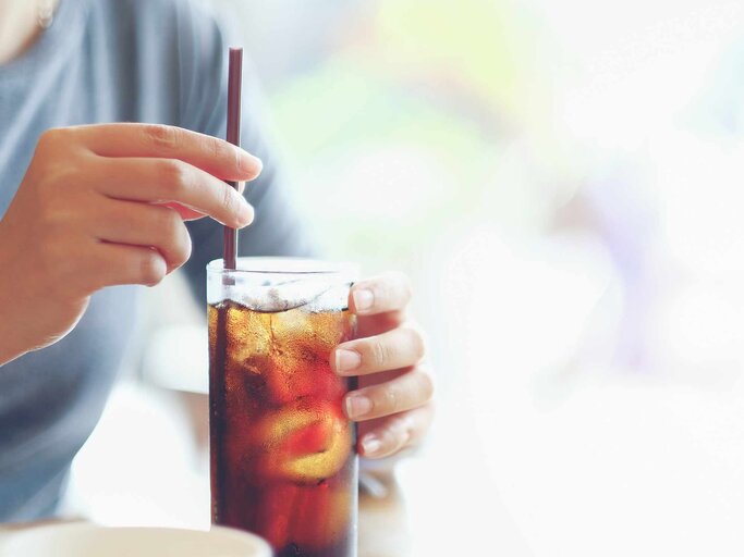 Frauenhand hält ein Glas Cola mit Strohhalm | © Getty Images/tongpatong