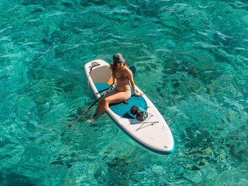 Frau sitzt auf einem Stand-up-Paddle-Board im Wasser | © Adobe Stock/Uldis Laganovskis
