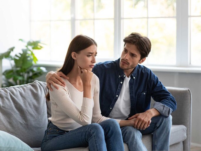 Paar sitzt gemeinsam auf der Couch. Mann tröstet Frau | © Getty Images/Prostock-Studio